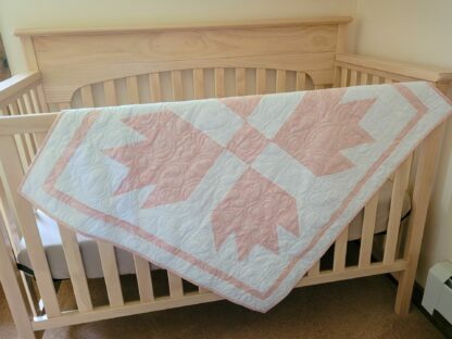 pink and white baby quilt draped over side of crib